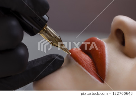 Cosmetologist makes permanent makeup on a woman's face. Specialist applies a tattoo on the patient's lips close-up Cosmetologist makes permanent makeup on a woman's face. Specialist applies a tattoo on the patient's lips close-up 122760643