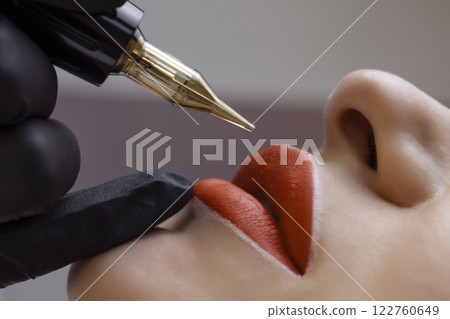 Cosmetologist makes permanent makeup on a woman's face. Specialist applies a tattoo on the patient's lips close-up Cosmetologist makes permanent makeup on a woman's face. Specialist applies a tattoo on the patient's lips close-up 122760649