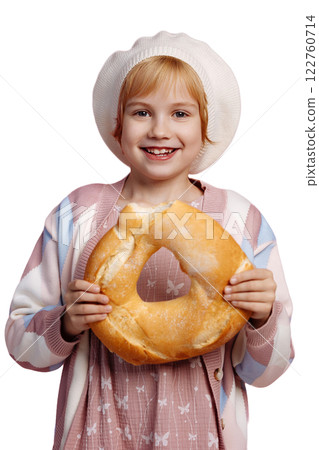 A child on a pink background in a chef's hat bites a large bagel. Look at camera. A child on a pink background in a chef's hat bites a large bagel. Look at camera. 122760714
