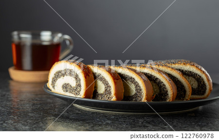 Poppy seed roll slices on a black plate. 122760978