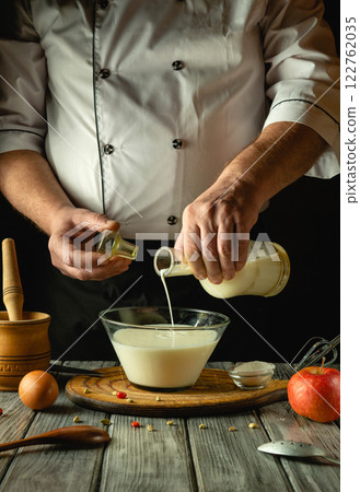 Hands skillfully pour fresh milk into a bowl, blending ingredients for a delicious recipe. The warm kitchen exudes a cozy ambiance, perfect for culinary exploration and flavor creation 122762035