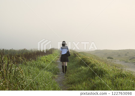 A high school girl walking along a coastal path shrouded in morning mist 122763098