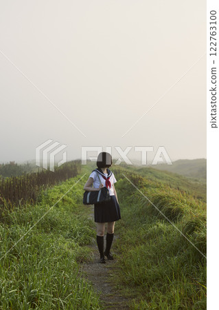 A high school girl walking along a coastal path shrouded in morning mist 122763100