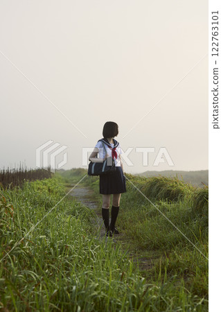 A high school girl walking along a coastal path shrouded in morning mist 122763101