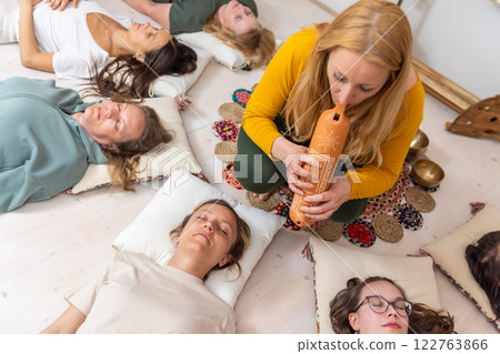 Group therapy session with Tibetan singing bowls for group of women lying on wooden floor surrounded by copper bowls. Meditation and relaxation 122763866
