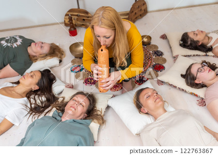 Group therapy session with Tibetan singing bowls for group of women lying on wooden floor surrounded by copper bowls. Meditation and relaxation 122763867