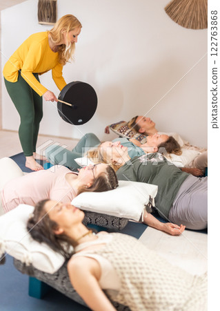 Group therapy session with Tibetan drum for group of women lying on wooden floor surrounded by copper bowls. Meditation and relaxation Group therapy session with Tibetan drum for group of women lying on wooden floor surrounded by copper bowls. Meditation and relaxation 122763868