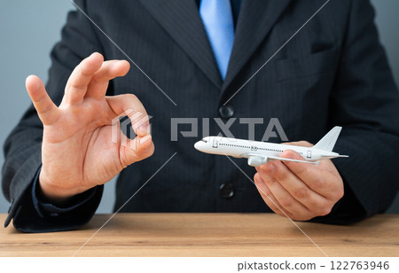 A man holds an airplane in his hands and shows the ok sign. Positive travel experiences. Flight safety, affordable airfare, smooth air travel, vacation planning, and airline promotions. 122763946