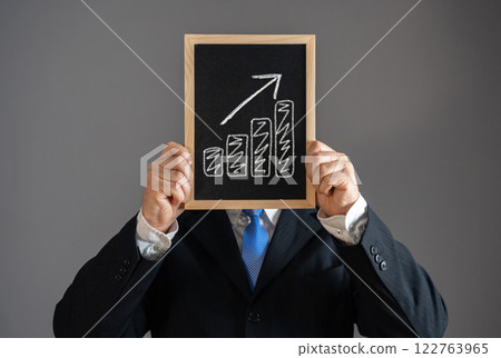 A businessman holds a sign with income growth in the place of his face level. Salary growth, economic success, investment returns, career advancement. Financial independence. Economic empowerment. 122763965
