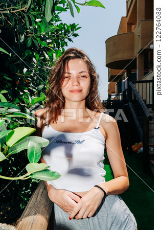 A young woman stands among lush green leaves, her hair flowing in the breeze, exuding confidence and A young woman stands among lush green leaves, her hair flowing in the breeze, exuding confidence and 122764088