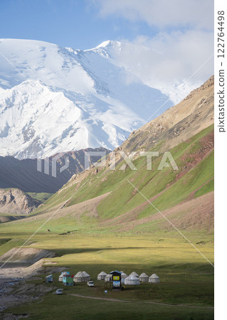 Vertical shot of nomadic campsite with yurts, massive snowy Pamir Mountains in backdrop, Kyrgyzstan 122764498