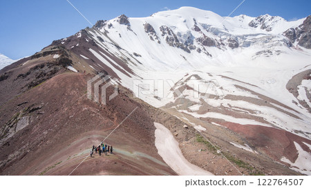 Group of hikers taking break in mountain saddle under snowy ridgeline, Pamir Mountains, Kyrgyzstan 122764507