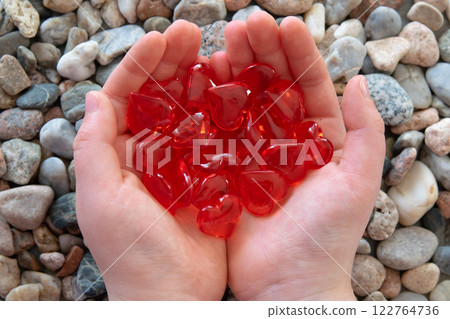 Much red bright glass hearts in child hands on the stones background. Concept of Valentine's day and romantic love. 122764736