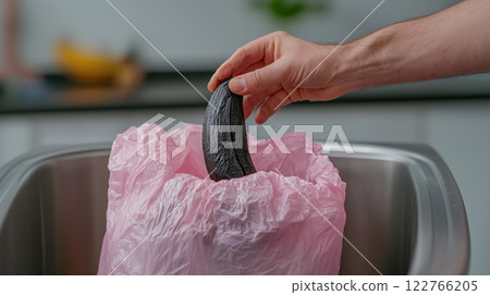 A hand dropping a blackened banana peel into a trash bin 122766205