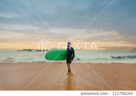 Young handsome male surfer with a surfboard is enjoying a view while walking a sandy beach at sea. Summer, vacation, ocean Young handsome male surfer with a surfboard is enjoying a view while walking a sandy beach at sea. Summer, vacation, ocean 122766264