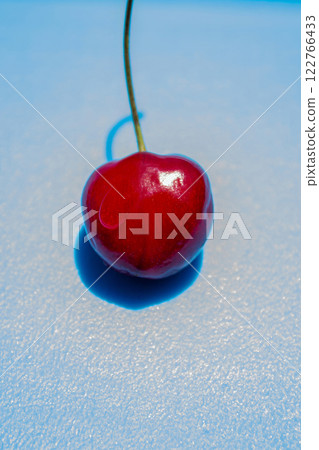 A cherry is sitting on a blue surface. The cherry is red and shiny A cherry is sitting on a blue surface. The cherry is red and shiny 122766433