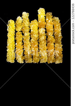 A row of yellow sticks with a black background. The sticks are made of sugar and are arranged in a line 122766436