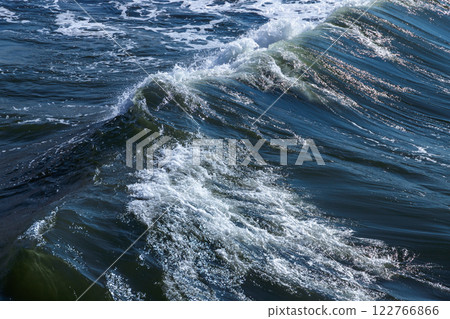 Sea wave with white foam goes over deep blue water 122766866