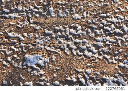 Sand covered with melting snow on a beach. Frozen ground pattern 122766961