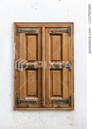 Old window with closed wooden shutters in white wall 122766990