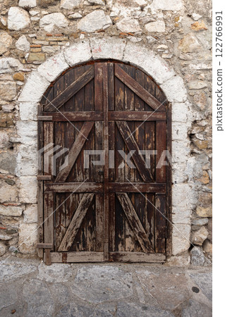 Old dark brown wooden door with arch is in an ancient stone wall 122766991