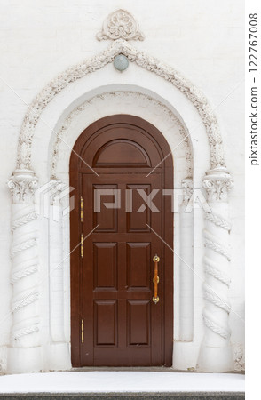 An old wooden door is in white wall of an ancient church, front view 122767008