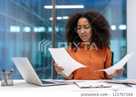 Dissatisfied and upset woman checking reports and financial documents, financier disappointed with performance results. Businesswoman doing paperwork inside office at workplace. 122767268