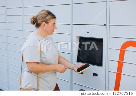 Parcel delivery machine. Mail delivery and post service concept. Happy smiling woman with phone at outdoor automated parcel machine. Electronic locker for storing parcels. 122767519