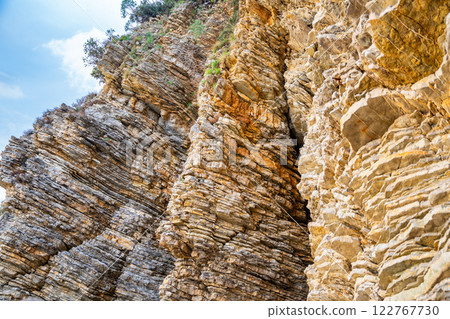 Layered rock texture in Budva, Montenegro. Sedimentary rocks with rugged surface of gray and brown. Natural formation of layers and cracks, geological structure. Layered rock texture in Budva, Montenegro. Sedimentary rocks with rugged surface of gray and brown. Natural formation of layers and cracks, geological structure. 122767730