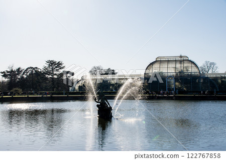 Stonework and fountain in the pond in front of a large glass greenhouse at Kew Gardens, outside London 122767858
