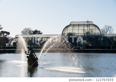 Stonework and fountain in the pond in front of a large glass greenhouse at Kew Gardens, outside London 122767859