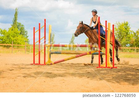 Jockey young girl doing horse jumping through hurdle 122768050