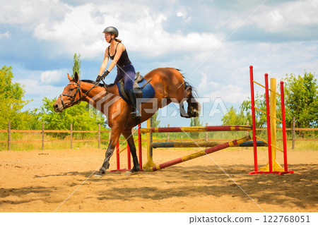 Jockey young girl doing horse jumping through hurdle Jockey young girl doing horse jumping through hurdle 122768051