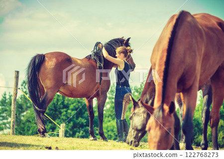 Jockey woman walking with horse on meadow 122768273