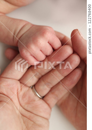 Close-up little hand of child and palm of mother and father. The newborn baby has a firm grip on the parent's finger after birth. A newborn holds on to mom's, dad's finger.  Close-up little hand of child and palm of mother and father. The newborn baby has a firm grip on the parent's finger after birth. A newborn holds on to mom's, dad's finger.  122768400