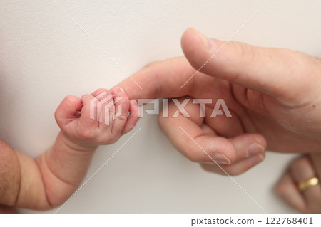 Close-up little hand of child and palm of mother and father. The newborn baby has a firm grip on the parent's finger after birth. A newborn holds on to mom's, dad's finger.  122768401