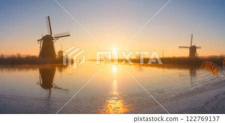Windmills in the Netherlands during sunrise. Foggy morning and sunshine. Dutch canals. Windmills in the Netherlands during sunrise. Foggy morning and sunshine. Dutch canals. 122769137