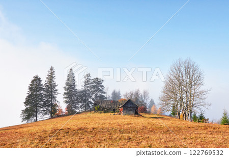 Sunrise above the high mountain foggy valley with old wooden houses on a hill in a mountain forest 122769532