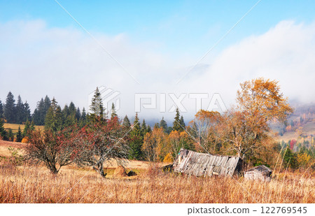 Sunrise above the high mountain foggy valley with old wooden houses on a hill in a mountain forest 122769545