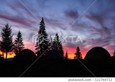 Majestic sky, pink cloud against the silhouettes of pine trees in the twilight time, tents on the front. Carpathians, Ukraine, Europe. Discover the world of beauty 122769712
