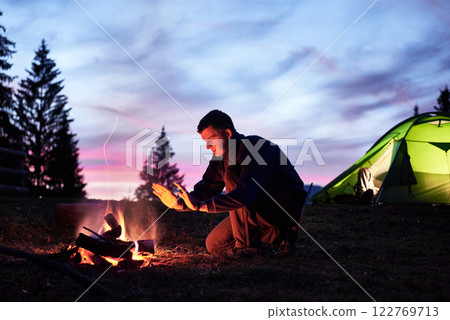 Hiking tourist have a rest in his camp at night near campfire 122769713