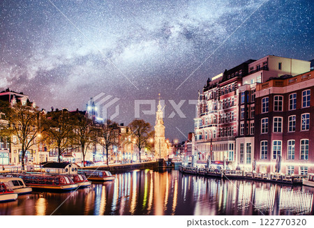 Beautiful night in Amsterdam. Night illumination of buildings and boats near the water in the canal. 122770320
