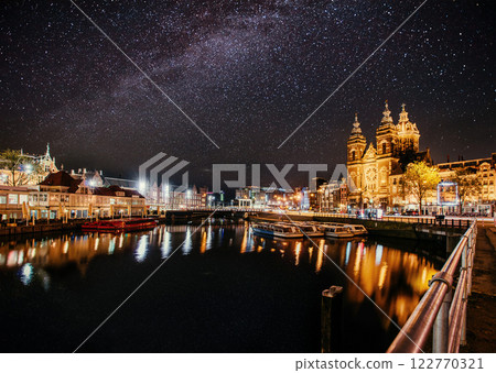 Beautiful night in Amsterdam. Night illumination of buildings and boats near the water in the canal. 122770321