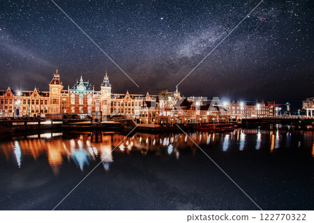 Beautiful night in Amsterdam. Night illumination of buildings and boats near the water in the canal. 122770322