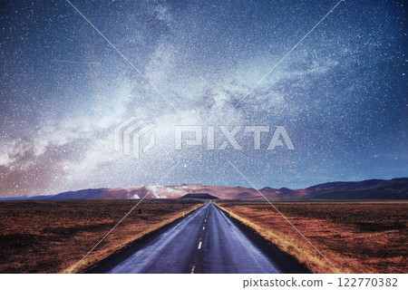 Starry Sky over the mountains. The asphalt road with white markings. Beautiful summer landscape. Soft filtering effect. Iceland Starry Sky over the mountains. The asphalt road with white markings. Beautiful summer landscape. Soft filtering effect. Iceland 122770382
