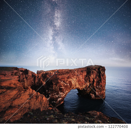 Cape Dyrholaey at southern Iceland. Altitude 120 m, and mean hill island with a door opening. Vibrant night sky with stars and nebula and galaxy. Deep sky astrophoto Cape Dyrholaey at southern Iceland. Altitude 120 m, and mean hill island with a door opening. Vibrant night sky with stars and nebula and galaxy. Deep sky astrophoto 122770408