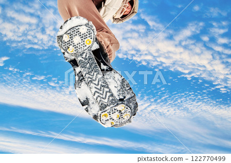 Traction device rubber base, metal studs and patterned tread enhances grip on ice or snow, low perspective on sky background. Traction device rubber base, metal studs and patterned tread enhances grip on ice or snow, low perspective on sky background. 122770499