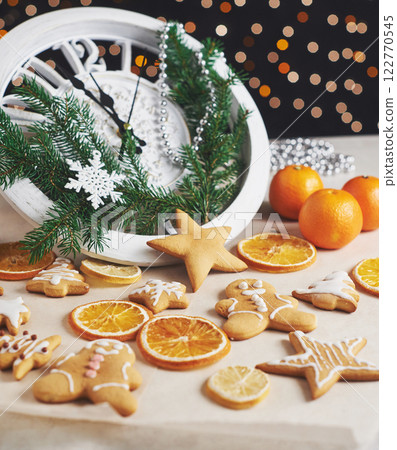 Happy New Year at midnight 2018, Old wooden clock with holiday lights and fir branches. Cooking and decorating christmas gingerbread cookies and fried orange slices Happy New Year at midnight 2018, Old wooden clock with holiday lights and fir branches. Cooking and decorating christmas gingerbread cookies and fried orange slices 122770545