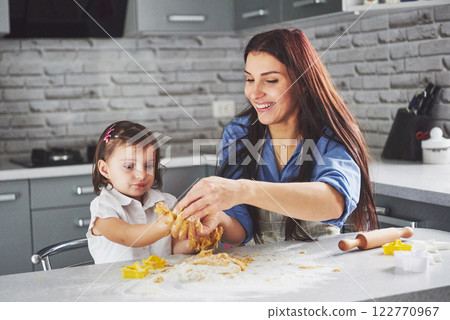 Happy family in the kitchen. Holiday food concept. Mother and daughter preparing the dough, bake cookies. Happy family in making cookies at home. Homemade food and little helper Happy family in the kitchen. Holiday food concept. Mother and daughter preparing the dough, bake cookies. Happy family in making cookies at home. Homemade food and little helper 122770967