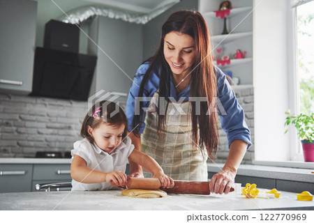 Happy family in the kitchen. Holiday food concept. Mother and daughter preparing the dough, bake cookies. Happy family in making cookies at home. Homemade food and little helper 122770969